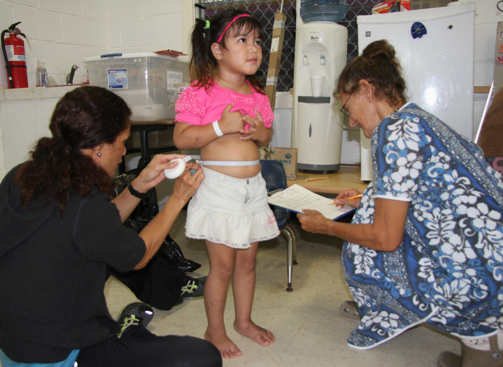 Ursula Teo Martin (left) and Agnes Vargo measure the waist circumference of a Head Start student. This parameter, along with body mass index (BMI), is used to assess whether the children are growing at a healthy rate or gaining weight too rapidly for their age.
